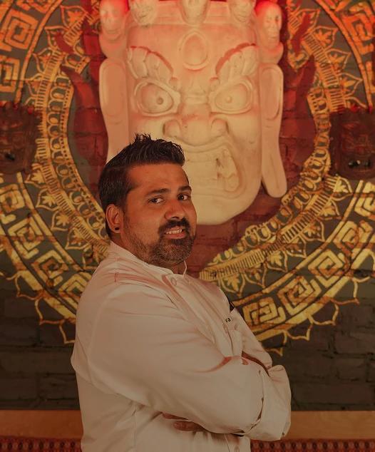 Chef Shiva Nepal standing before traditional Nepali artwork
