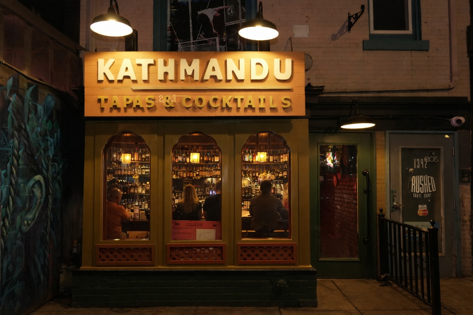 Elegant restaurant interior with warm ambient lighting, wooden tables set with white linens, and traditional Nepalese decorative elements on exposed brick walls